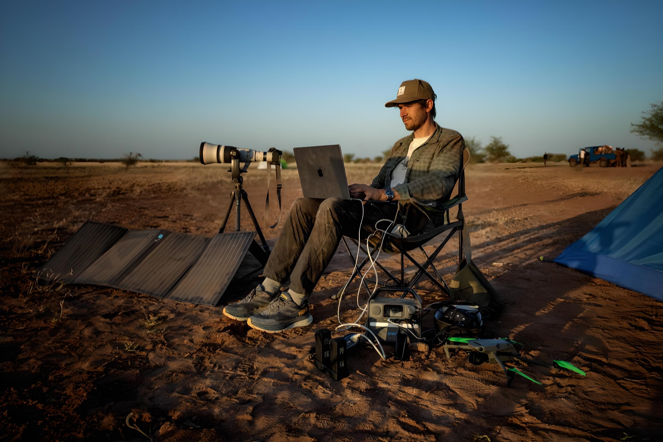 Man working on laptop powered by portable solar panel and battery pack in remote outdoor location.